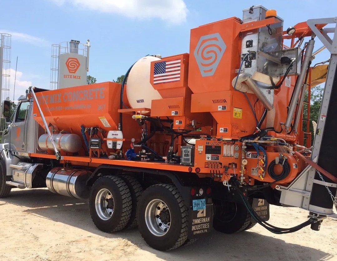 An orange SiteMix truck delivers ready made concrete to a construction site